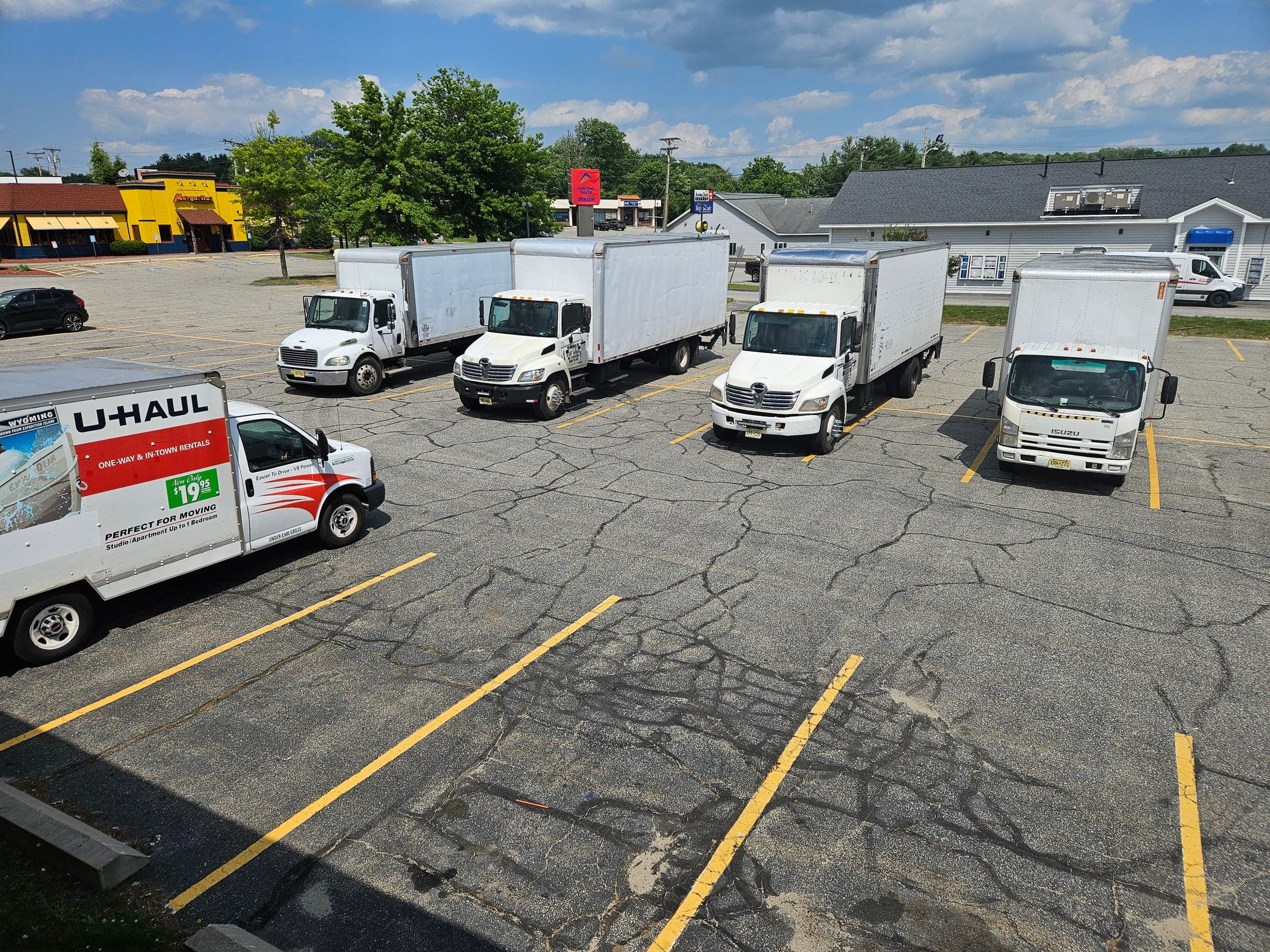 Saffron Inn parking lot on a summer weekday — five contractor box trucks and a U-Haul rental parked across the lot, Auburn Maine