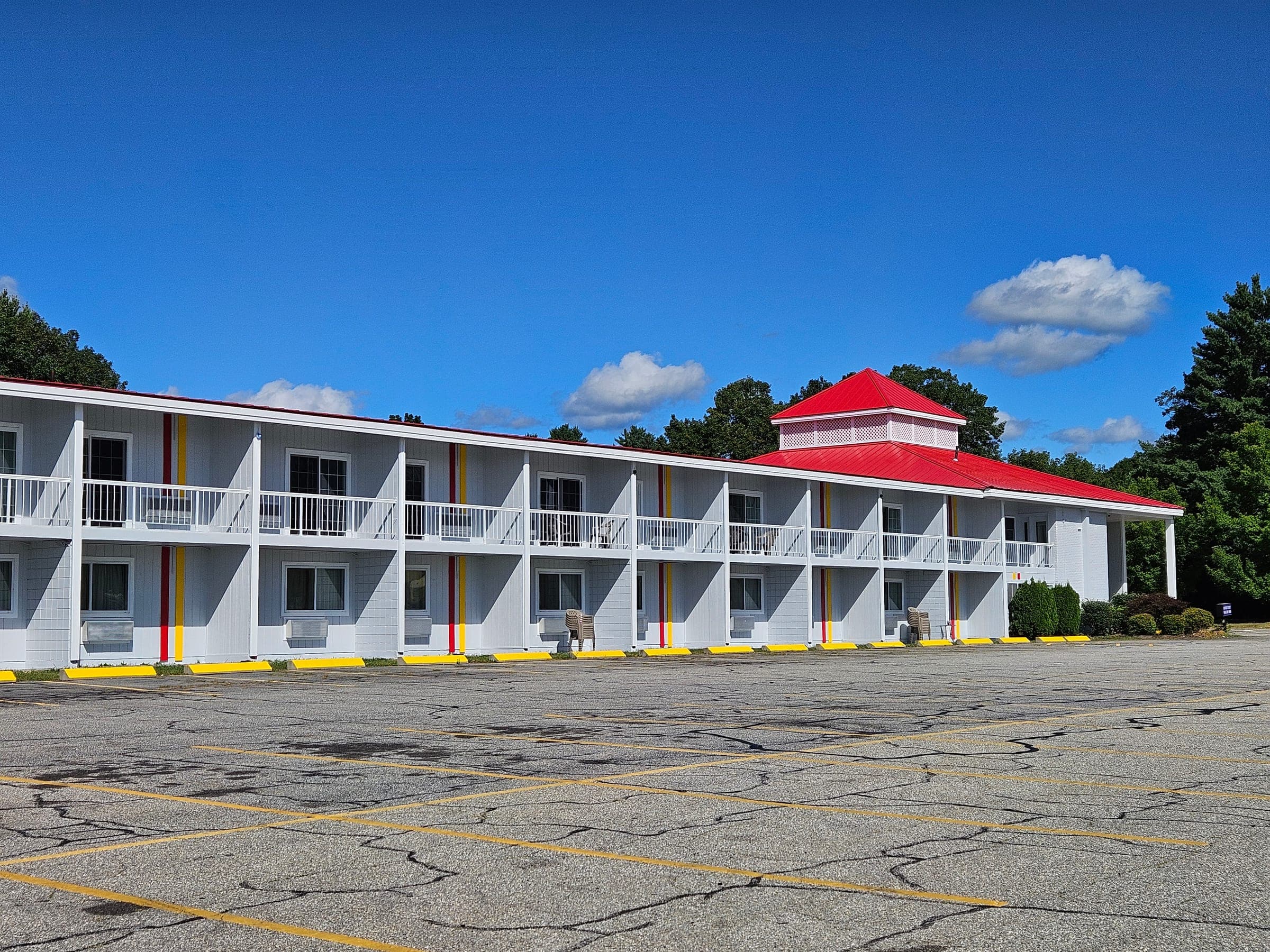 Saffron Inn front exterior on a summer afternoon, two-story motel with white siding, red trim, second-floor balconies, and red cupola roof, Auburn Maine