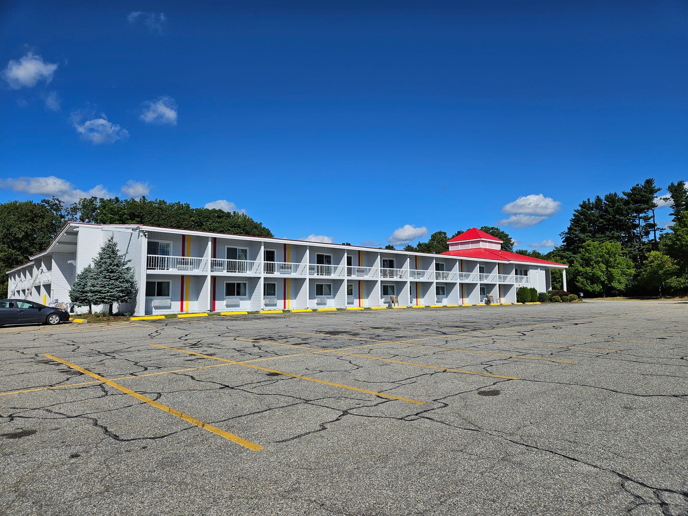 Saffron Inn exterior in summer, wide angle showing the full two-story motel with red cupola roof and second-floor balconies, Auburn Maine
