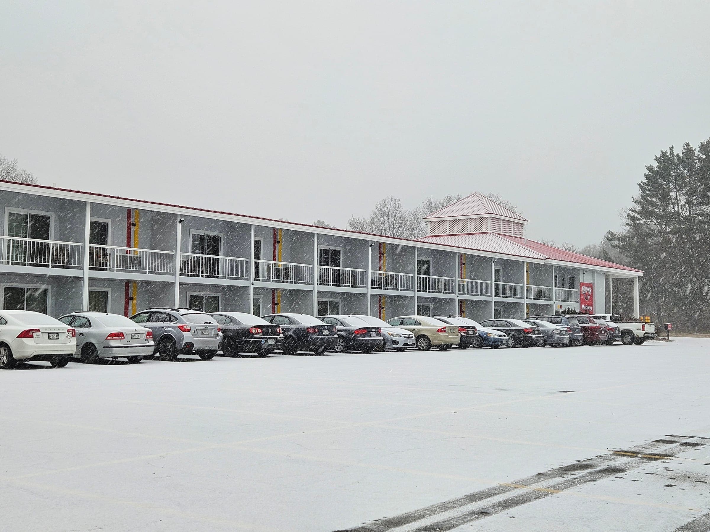 Saffron Inn exterior in falling snow, two-story motel with cars in the parking lot during a winter storm, Auburn Maine